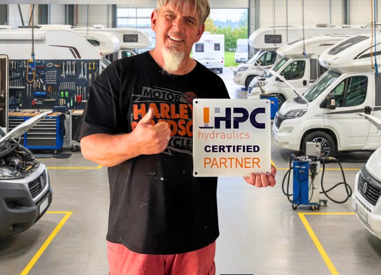 Mike Ebert mit dem HPC-hydraulics-Partnerschild in der Werkstatt
